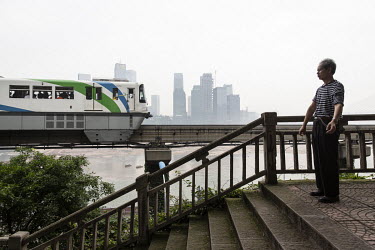 A CRT (Chongqing Rapid Transit) monorail train passes an elderly man doing his morning exercises on the banks of the Jialing River.