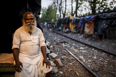 A man sits outside a shelter in a slum built along the railway tracks.