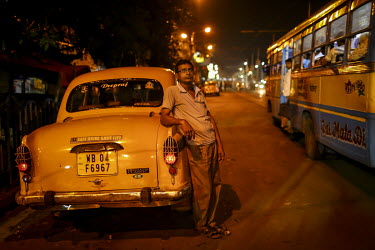 A taxi driver stands beside his vehicle parked at the roadside.