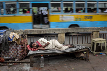 A public bus drives past a man sleeping on a bench beside a road.
