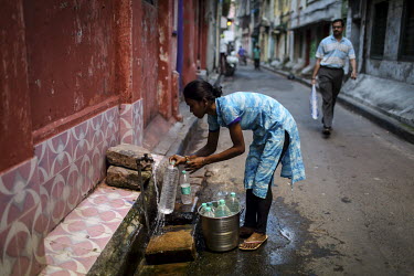 A young woman fills plastic bottles with water from a public standpipe.