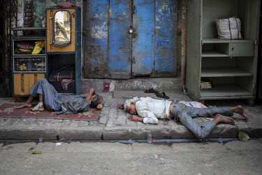 Two men sleep on the pavement.
