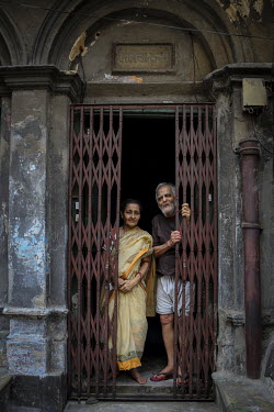 AN elderly couple look out from the shuttered doorway of a building.