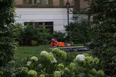 A construction worker looks at his mobile phone while taking a break in a small lush park in the City of London.