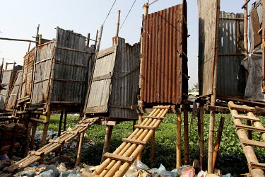 A row of toilets raised on stilts and made from galvanised metal stand among rubbish strewn beneath them.