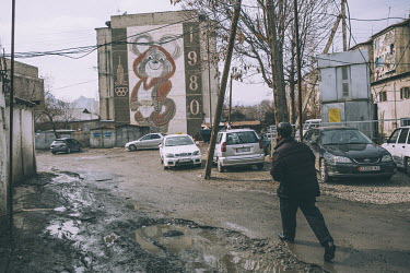 A man walks on a street near a mural made for the 1980 Moscow Olympics.