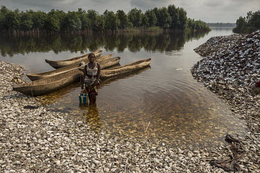 A woman stands on mounds of clam shells on the banks of one of the many water channels that run among the mangrove forest. Women dive as deep as four metres to collect the clamps that they sell on ske...