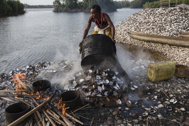 A man empties a metal vessel of clams after they have been cooked. People make skewers of the clam meat to sell in nearby cities. They are collected by hand from the beds of the many water channels th...
