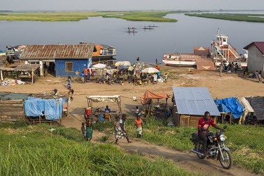 A man rides a motorcycle up a hill where a ferryboat is moored on the banks of the Mfimi or Fimi river.