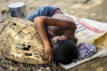 A boy, working as a day labourer unloading aggregates for the construction industry from barges, sleeps on the riverbank during a break in his work.