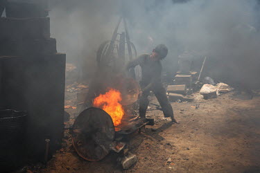 A child labourer, wearing no safety equipment, smelting metal while casting ship's propellors at a shipyard.