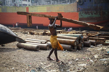 A labourer at a ship yard carries a piece of rusting metal salvaged from an old vessel.