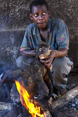 In Igende, a village on the Ruki River, a man burns fur off a monkey as it is prepared for market where they will be sold for around USD 20.00.
