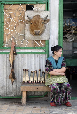 A woman sits beside a display of cow's feet and tripe at a butcher's shop.