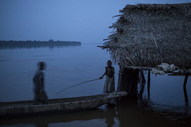 A boy fishing at dawn from a canoe (pirogue) moored on the Congo River.