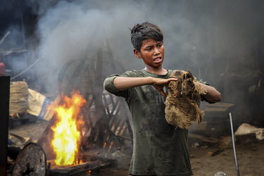 A child working in a shipyard wipes his hands on a piece of old hessian sacking.