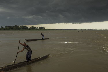 Men paddle their canoes (pirogues) towards home as fast as possible to avoid an incoming storm.