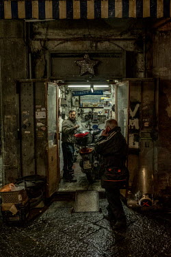 A mechanic busy with the maintenance of a scooter in his tiny workshop.