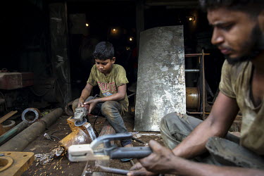 A child labourer uses an angle grinder to clean rust from a metal fitting in a workshop producing parts for the ship building industry. The boy has no visible protective equipment.