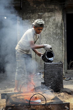 A child, working in a shipyard, pours oil into a drum close to where casting furnace fires are burning.