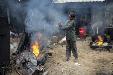 A child labourer tends to a furnace fire while casting metal fittings in a workshop producing parts for the ship building industry. The boy has no visible protective equipment.