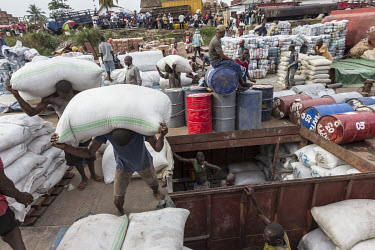 Porters load and unloaded cargo onto a barge moored in the harbour. In the background, bales of second-hand clothes that are collected in Europe and the US but sold in Congo, wait to be moved.