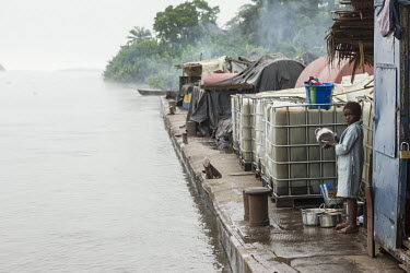 A young girl cleaning dishes in the early morning onboard a barge sailing up the Congo River.