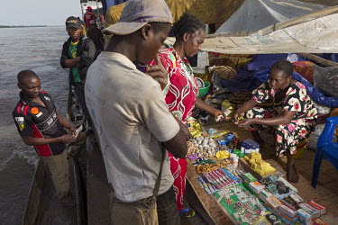 A woman buys medicines from a small stall on a barge sailing up the Congo River. Some passengers, or the wives of crew members, recouping their travel expenses or earn a living peddling wares to fishe...