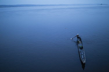 A lone fisherman crosses the river in a pirogue in the early morning mist.