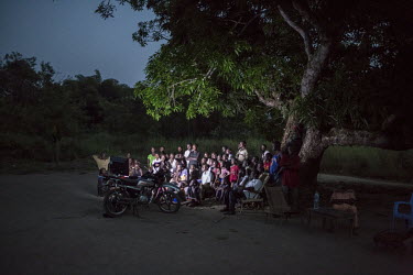 People gather around a television that has been set up beneath a tree in the village centre in order for residents to watch a football match.