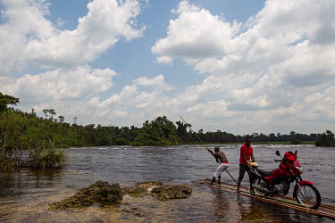 A bank employee who takes cash to outlying areas on a motorcycle crosses a river on board a wooden raft. The Congolese government has outsourced the payment of salaries to isolated employees to some o...