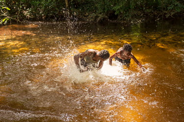 Two women having fun, in between washing clothes and rinsing manioc roots, splashing water in the shallows of a river.