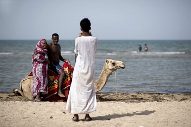 A Rashaida bedouin youth with camel takes a photo of an Eritrean couple who live overseas and are visiting the Gurgusum Beach Resort Hotel as tourists.