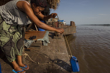 A woman travelling on a Congo River barge, collects water for cooking from the river.