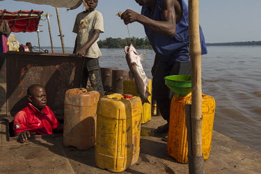 A fisherman selling a catfish to a man working on a Congo River barge.
