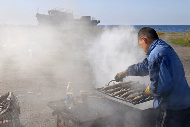 A man is grilling omul, a whitefish species of the salmon family endemic to Lake Baikal. It is considered a delicacy, but listed as an endangered species since 2004.