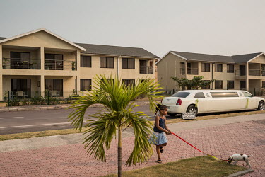 A limousine is parked on a street in front of new apartment buildings under construction at the 'Cite du Fleuve' gated community. A lone girl with her dog walk the empty streets. The development was b...