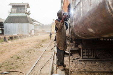 A man welding the hull of a ship at a shipyard on the banks of the Congo River.