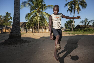A young man playing football with an improvised ball made of plant fibres.