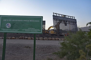 A sign indicates the border with the USA. Behind the sign a metal fence is being constructed at the border line.
