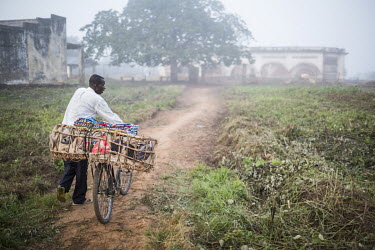 A man pushes his bicycle through early morning fog to sell his merchandise (mainly clothing) at a nearby market.