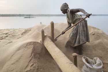 A woman searches a huge pile of rice husks for any grains that have been missed during the decortication process. In the background is the Congo River.