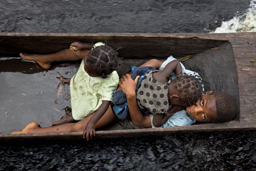 Two babies and their older brother travel in a watery canoe (pirogue) over the Itimbiri River.