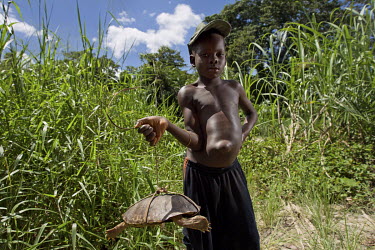 A boy with signs of malnutrition holds a turtle caught for consumption.