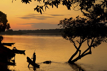 A man paddles a canoe (pirouge) at sunrise on the Aruwimi River.