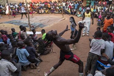A wrestler gets the crowd's attention from outside the ring. He is part of a travelling troupe of fighters who go from village to village putting on a show for the residents. They stay in each village...