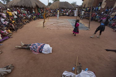 A wrestler lies beneath a sheet outside the ring in front of an eager crowd of spectators. He is part of a travelling troupe of fighters who go from village to village putting on a show for the reside...