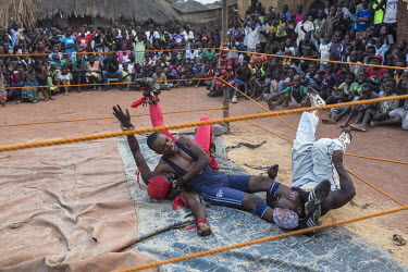 A wrestler grapples with two opponents inside the ring during a bout put on by a travelling troupe of fighters who go from village to village putting on a show for the residents. They stay in each vil...