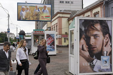 People in central Minsk, pass advertisements for Coca Cola, Versace and a patriotic propaganda poster.