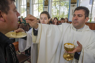Gaspal Marian, the priest at St. Michael's (Mihail) Catholic church, offers one of his congregation a wafer of sacramental bread during Holy Communion (Mass).